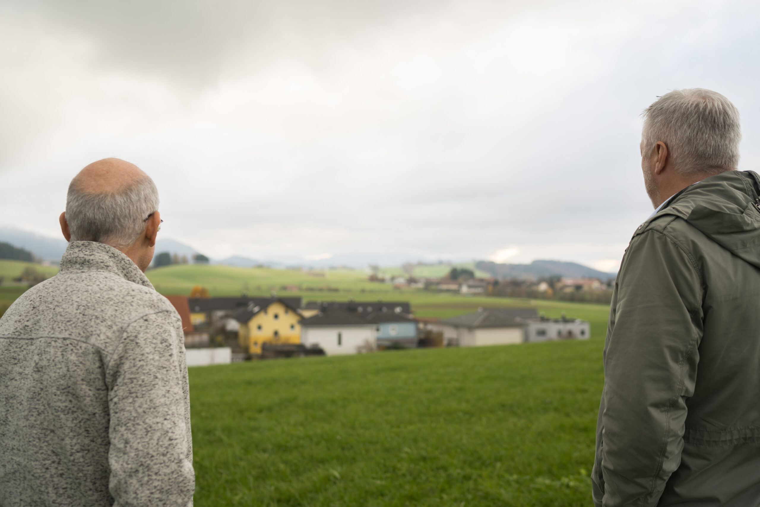 Zwei Mitarbeiter der Land-Invest stehen auf einer kleinen Anhöhe auf einer Wiese und schauen auf nahegelegene Häuser.