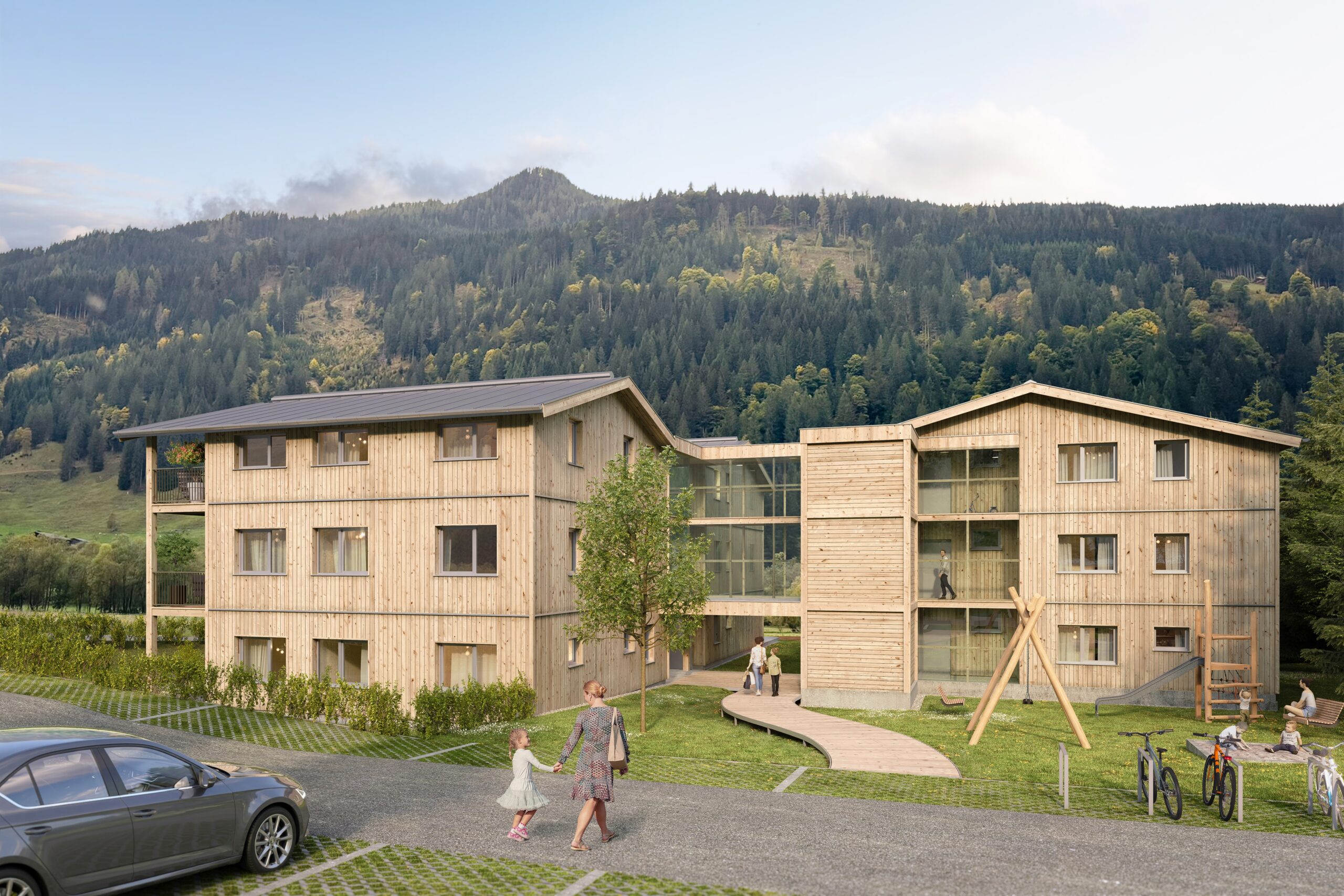 Architekten-Visualisierung von zwei miteinander verbundenen Mehrparteienhäusern in Holzbauweise, vor waldig-bergigem Hintergrund. Mehrere Personen mit Kindern sind auf dem Weg zum Haus, im Haus oder am vor dem Haus gelegenen Spielplatz.